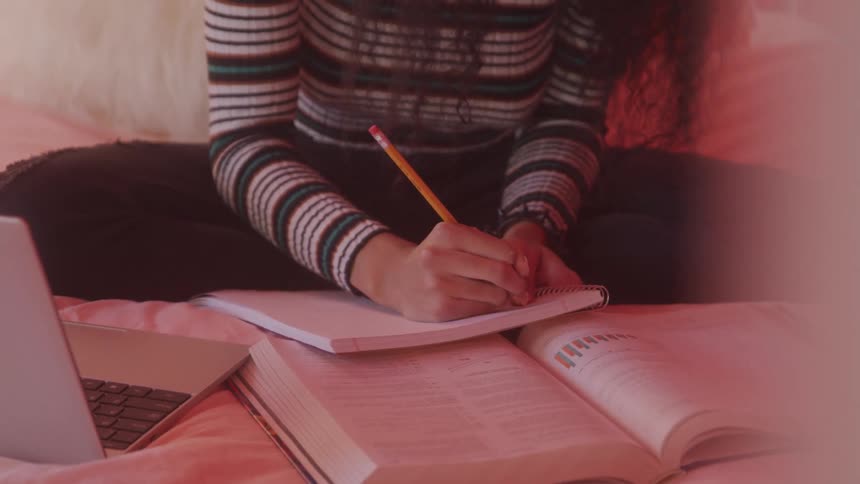 Person studying on bed with notebook laptop and open books