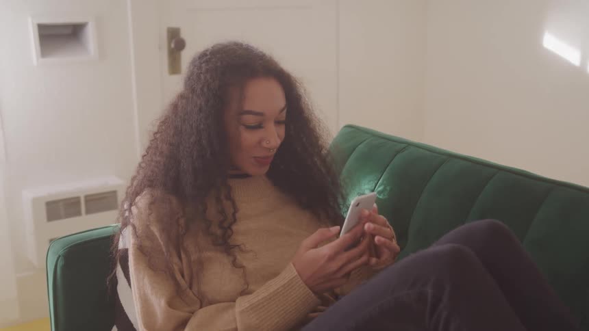 Teen girl relaxes on a couch smiling while on a video call