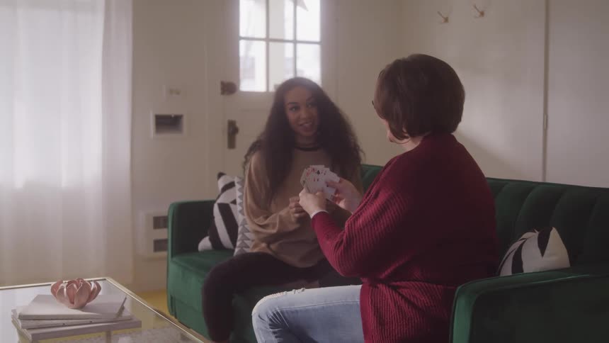 Mother and daughter enjoy a warm moment playing cards on the living room couch