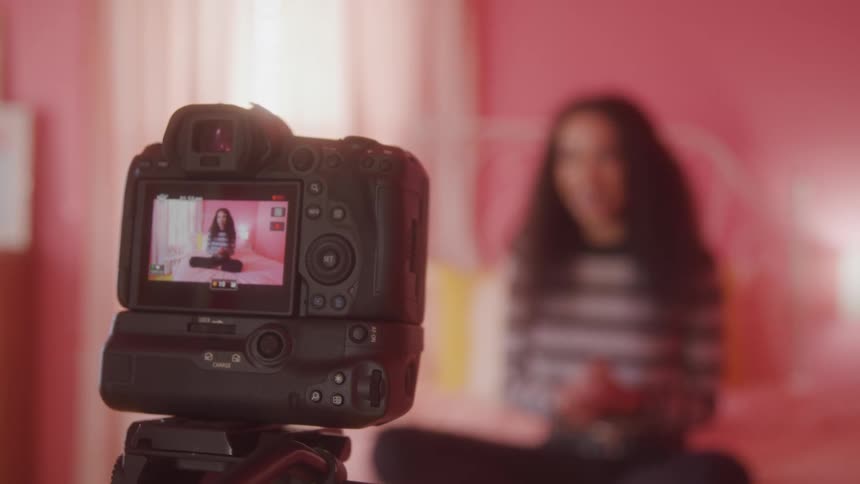 A woman in her room records a video vlog with her camera on a stand around midday