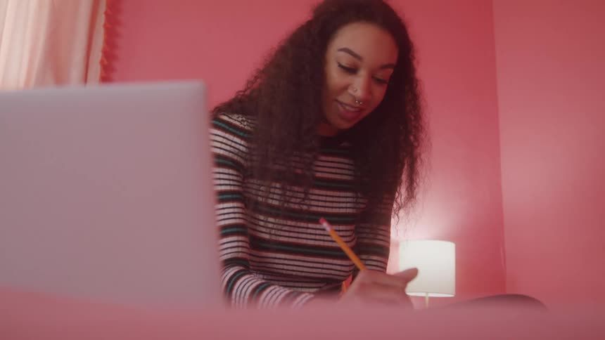 A woman is writing and smiling in front of her laptop