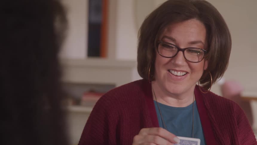 A woman smiles and laughs while playing cards with a friend