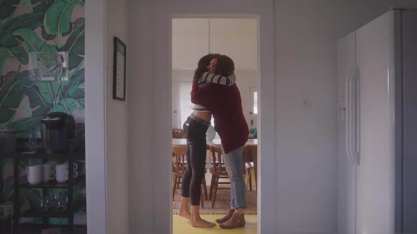 Two women inside a house hugging each other