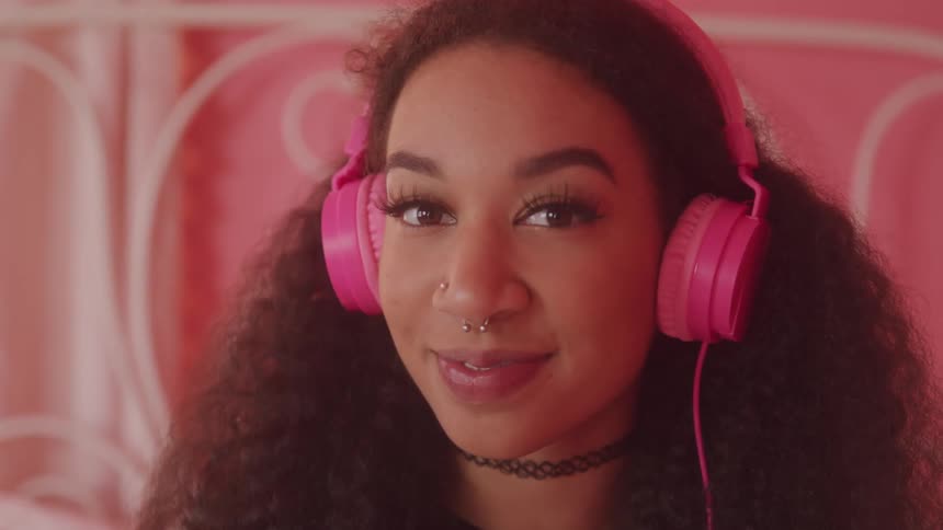 Portrait of young curly haired woman with happy facial expression and wearing pink headphones
