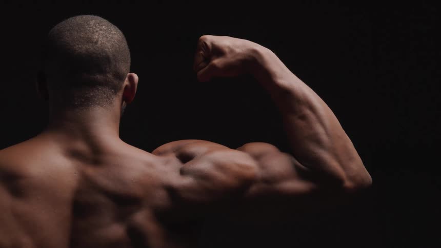 Close up from behind of a young black man flexing his right arm