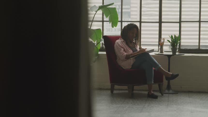 Woman sitting in a red armchair writing in a notebook