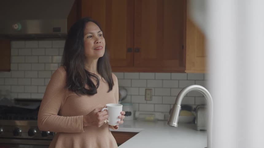 Woman with happy facial expression holding a mug while standing in the kitchen