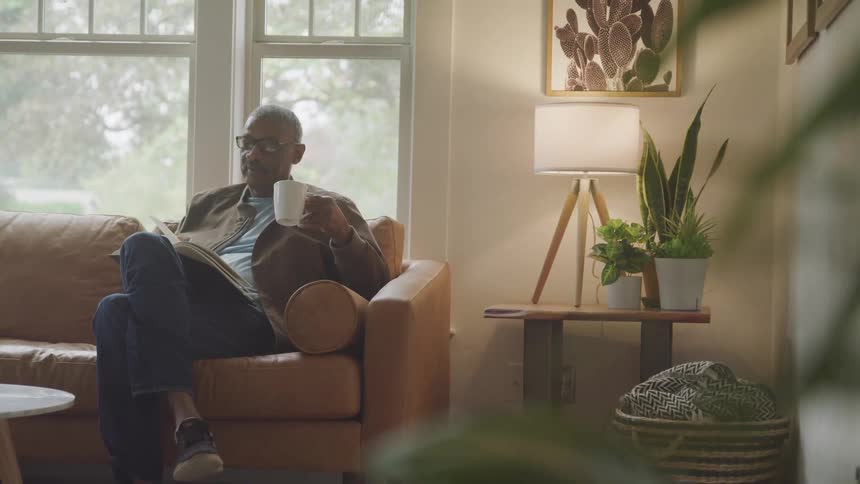 A man sits on the sofa reading and holding a hot drink