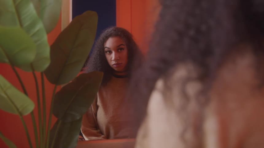 Woman with curly hair looking at herself in front of a mirror