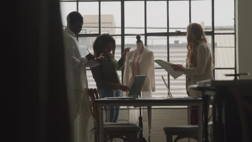 Three designers collaborate around a mannequin in a sunlit studio