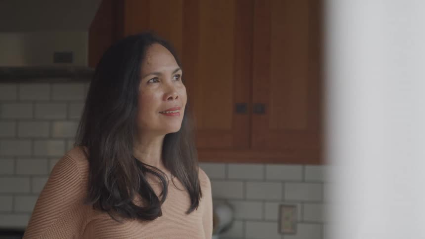 A woman stands in the kitchen with a smile on her face around midday