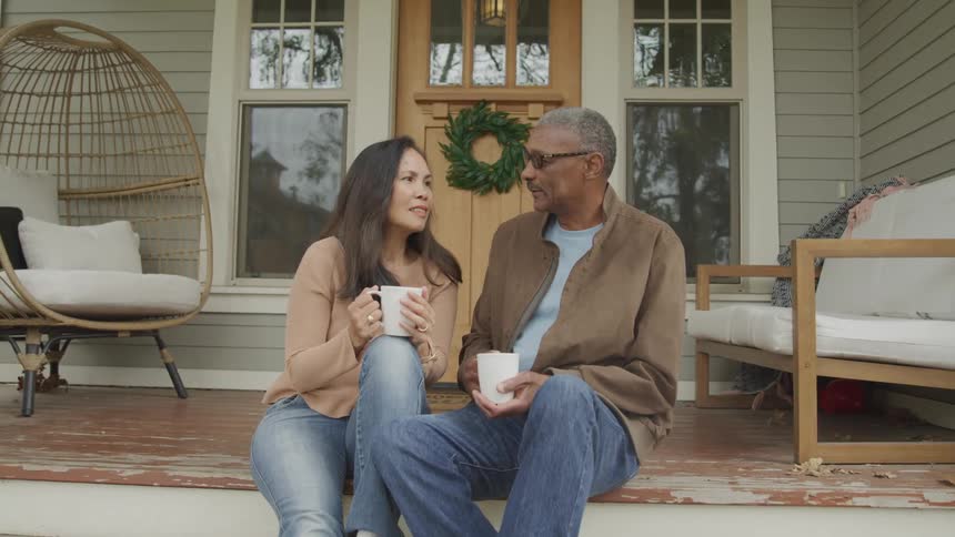 Couple sitting outside their house holding white mugs