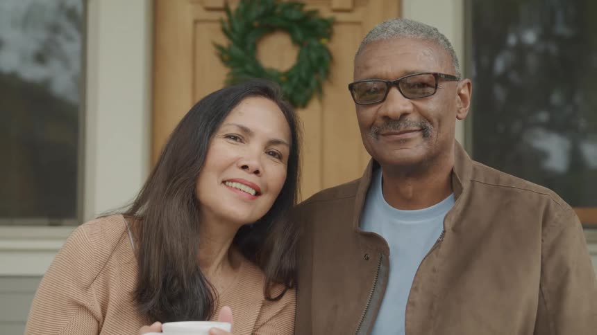 A smiling couple poses warmly together on a front porch