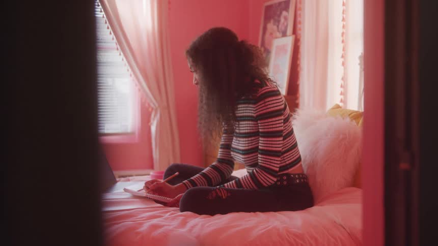 Woman sitting on bed with notebook and laptop open