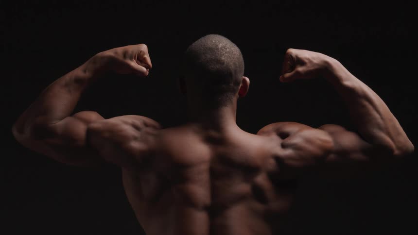 Back of a man flexing arms muscle in a dark room