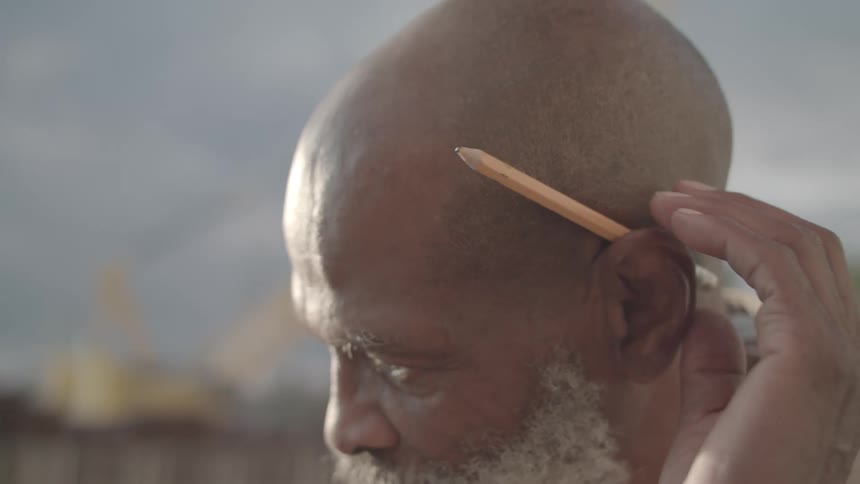 An elderly man takes a pencil from behind his ear
