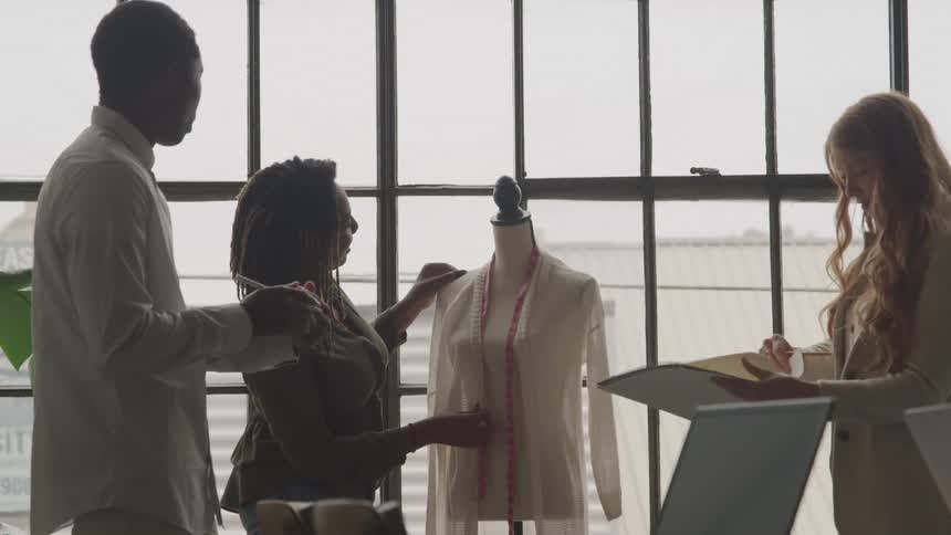 Three designers collaborate on a clothing mannequin in a fashion studio