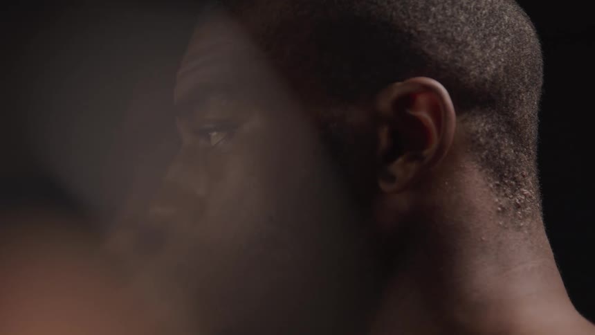 A closeup of the back of a mans head shows short hair against a dark background