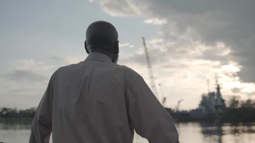 A man stands looking out at a ship on the water