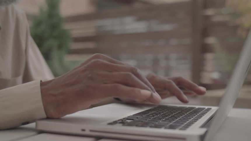 Close up of an elderly black man typing on a laptop computer in an office area during daytime