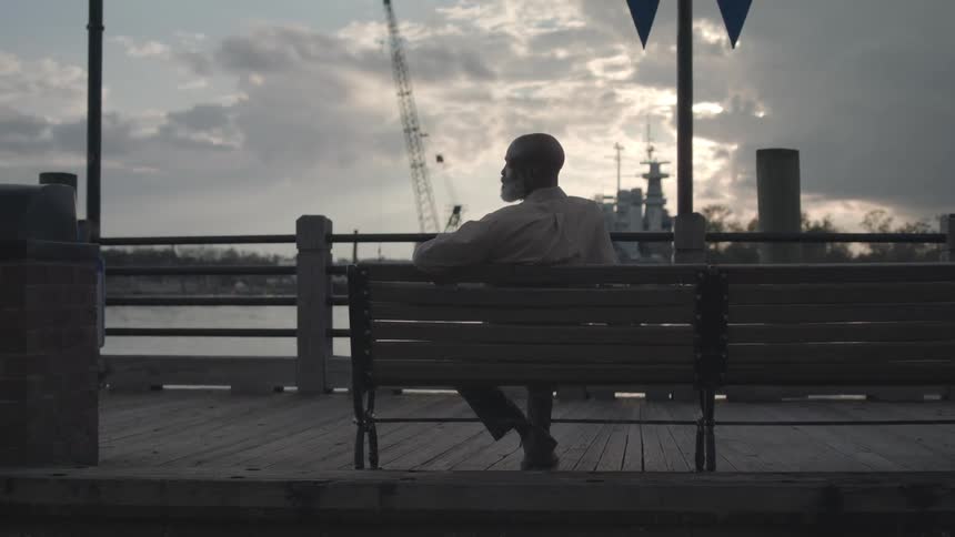 The man sits on the boardwalk looking at the shore