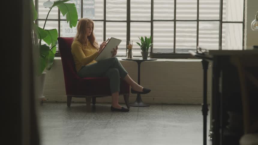 Woman holding a pencil on a board while sitting in a red armchair