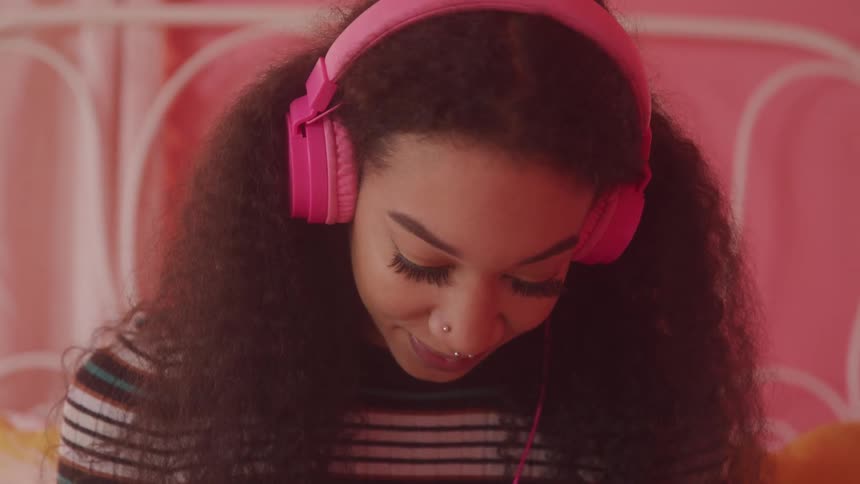 Curly haired woman looking down with pink headphones