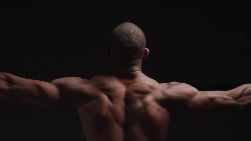 Close up of a young black mans nude back as he raises and flexes his arms