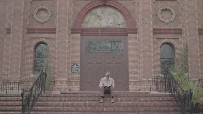 Man sitting on a ladder in an outdoor setting with a book