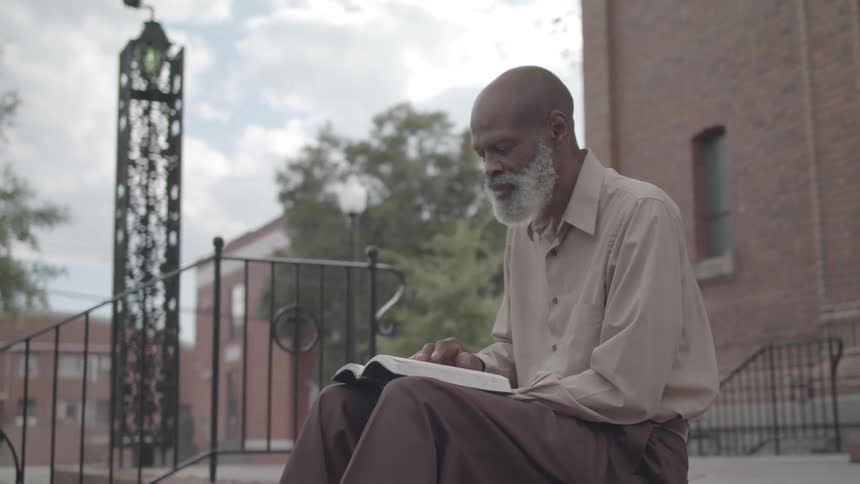 Elderly man reads a book quietly on outdoor steps