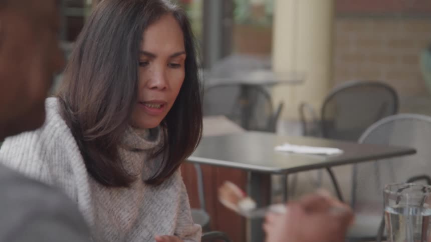 Two people are casually talking while eating at an outdoor cafe