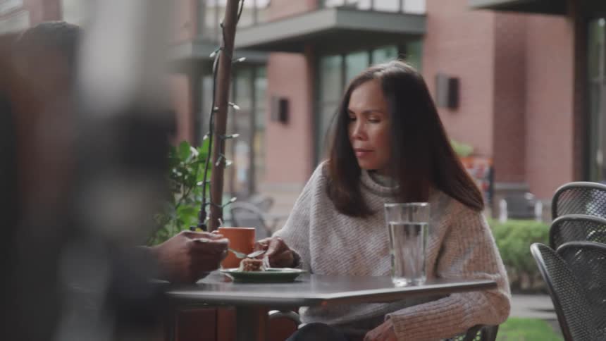 Two people sit at an outdoor cafe table engaged in a calm conversation over drinks and dessert
