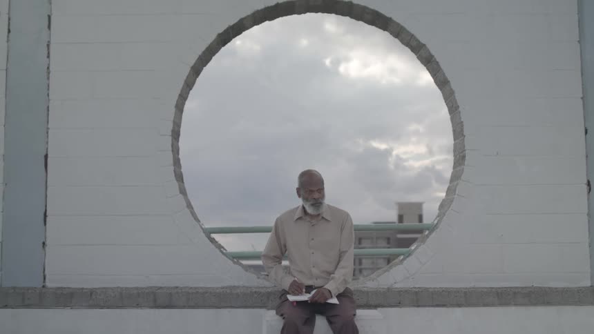 Elderly man sketches while gazing through a circular wall opening