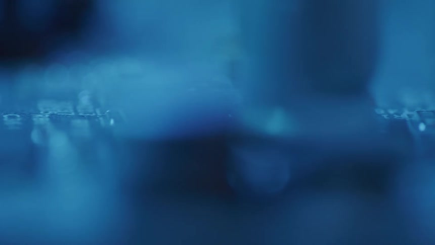 A computer circuit board is shown in extreme detail its components and pathways bathed in a cool blue light