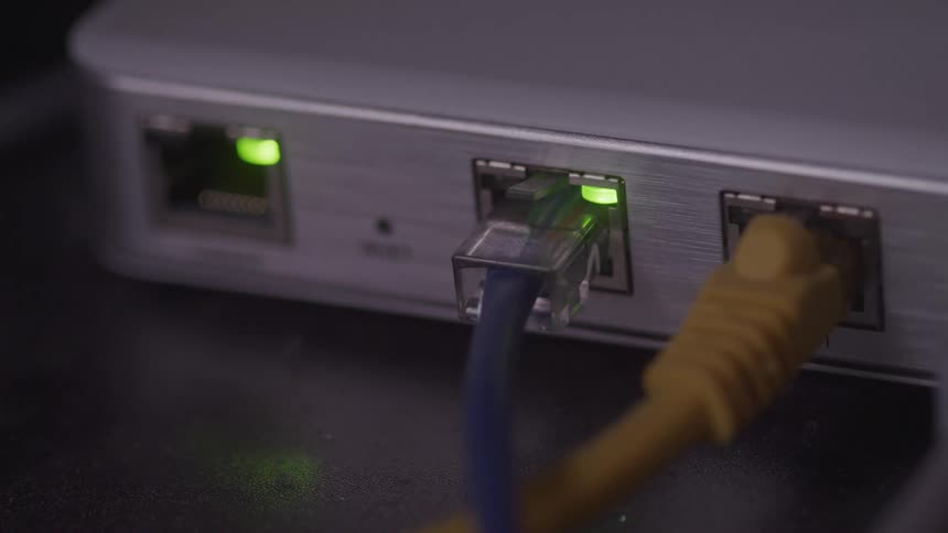 An extreme closeup shows blue and yellow ethernet cables plugged into a network device as green led lights blink to indicate data activity