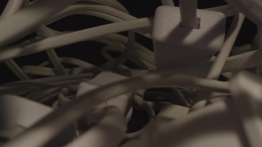 A pile of white tangled cables rests on a dark surface