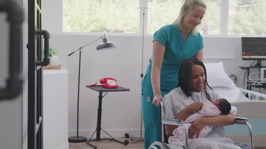 Nurse carrying a mother with a newborn baby in her arms with the help of a wheelchair