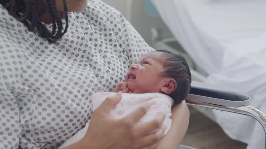 A woman wearing a patterned gown holds a swaddled baby
