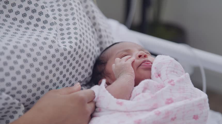 A newborn baby is held by the mother in the hospital