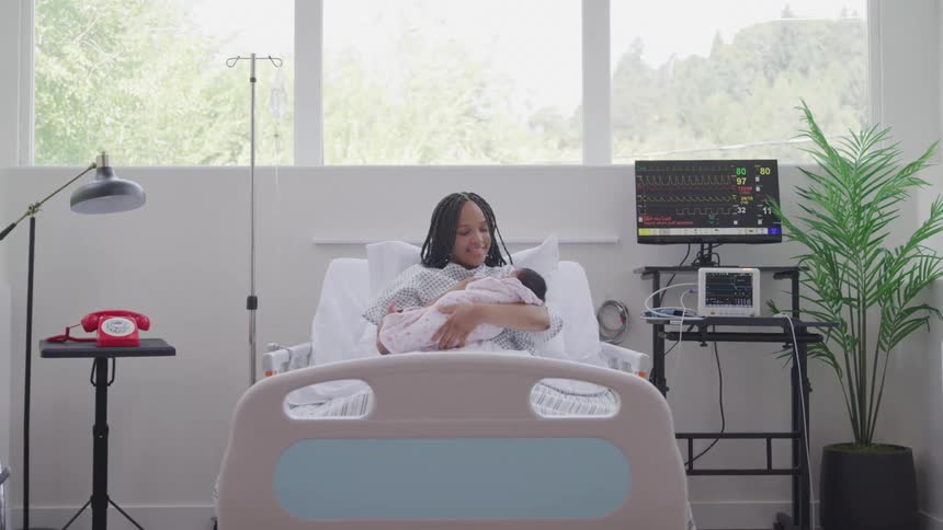 A joyful mother smiles warmly while cradling her newborn in a hospital bed