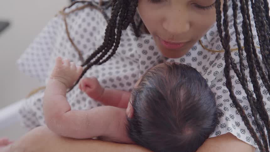 New mother wearing a hospital gown kissing her newly born baby