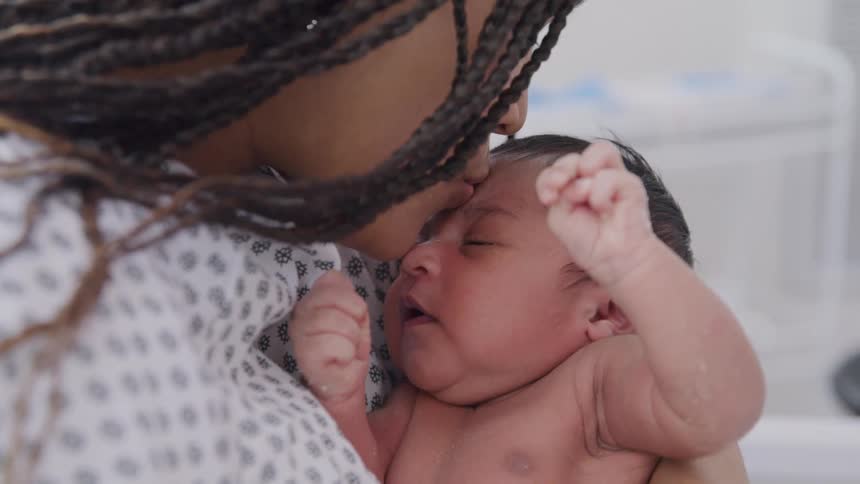 New mother in a hospital bed kissing her newborn on the forehead