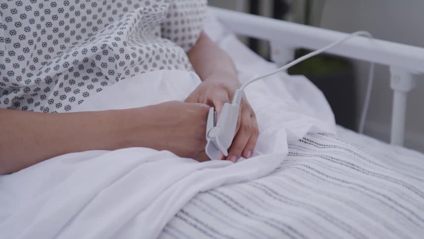 Close up of a woman lying on a hospital bed with a pulse oximeter fixed to her index finger
