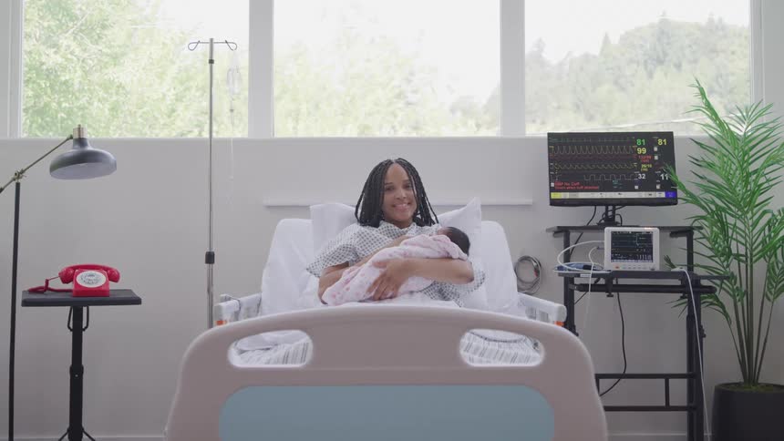 Cheerful mother holding newborn baby boy while lying in a hospital bed