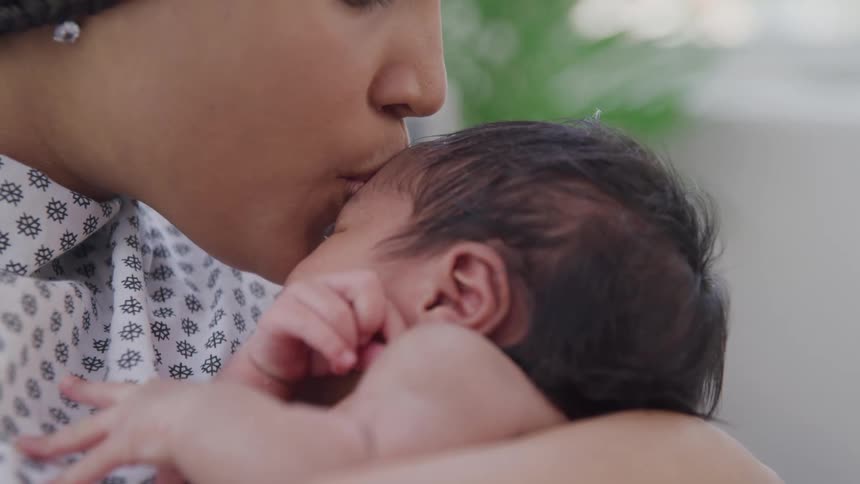 A mother who just gave birth kisses her baby in her arms around midday in the hospital