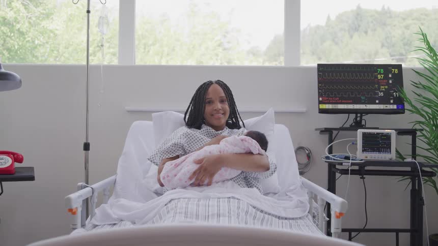 Mother lying in a hospital bed with a newborn baby in her arms