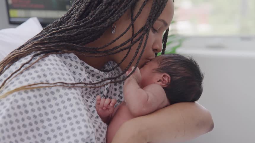 A young woman with braids cares for her newborn baby in the hospital around midday