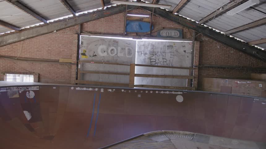 An indoor skate park features a graffiticovered halfpipe ramp beneath exposed beams and hanging lights