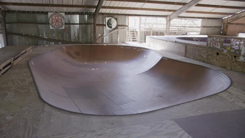 A bowl is located in an empty indoor skate park around midday