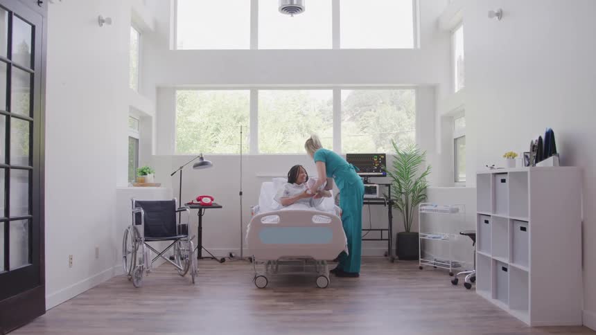 A nurse gently hands a newborn baby to a mother sitting in a hospital bed